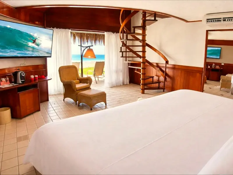 Cama do bangalô com poltrona e escada caracol, com o mar visto pela porta