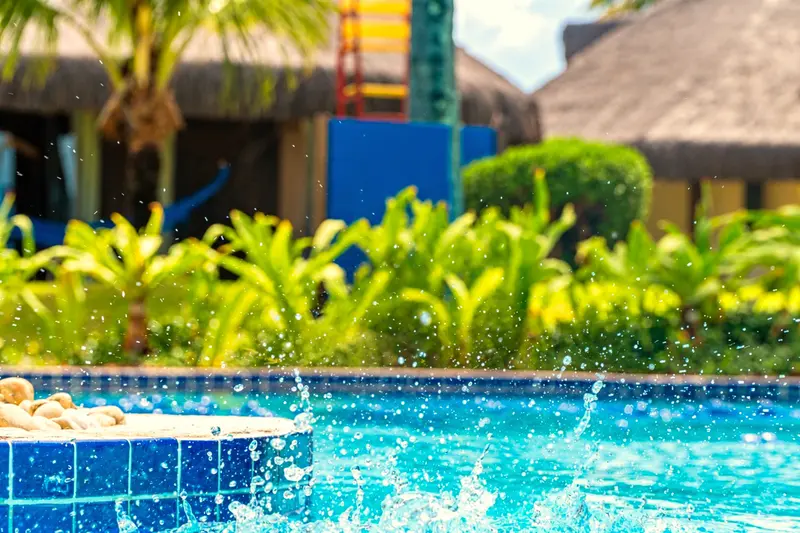 Borda da piscina com respingos e jardim tropical ao fundo