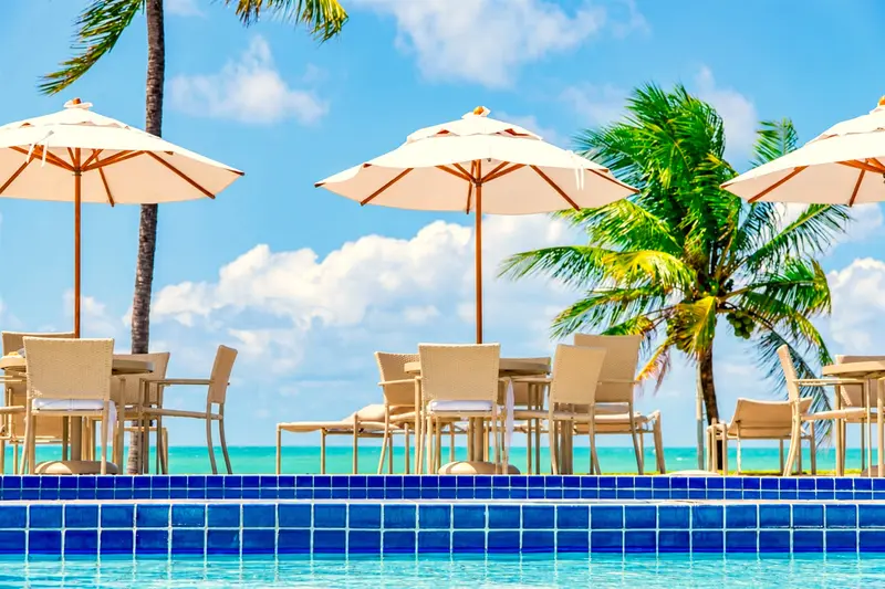 Mesas sob guarda-sóis à beira da piscina, com o mar ao fundo