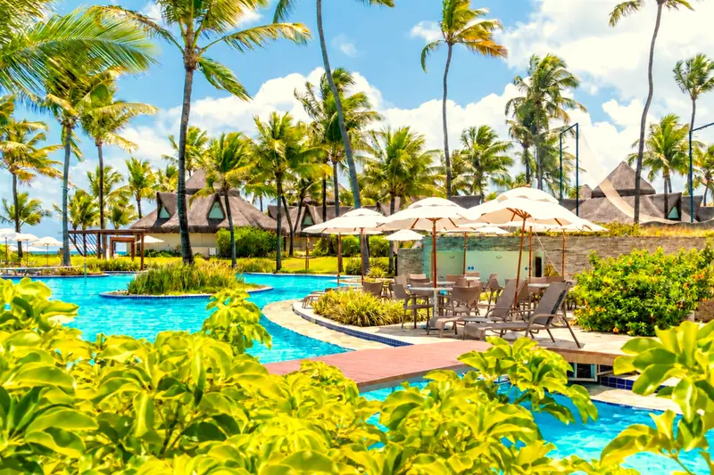Piscina sinuosa entre jardins tropicais, guarda-sóis e coqueiros