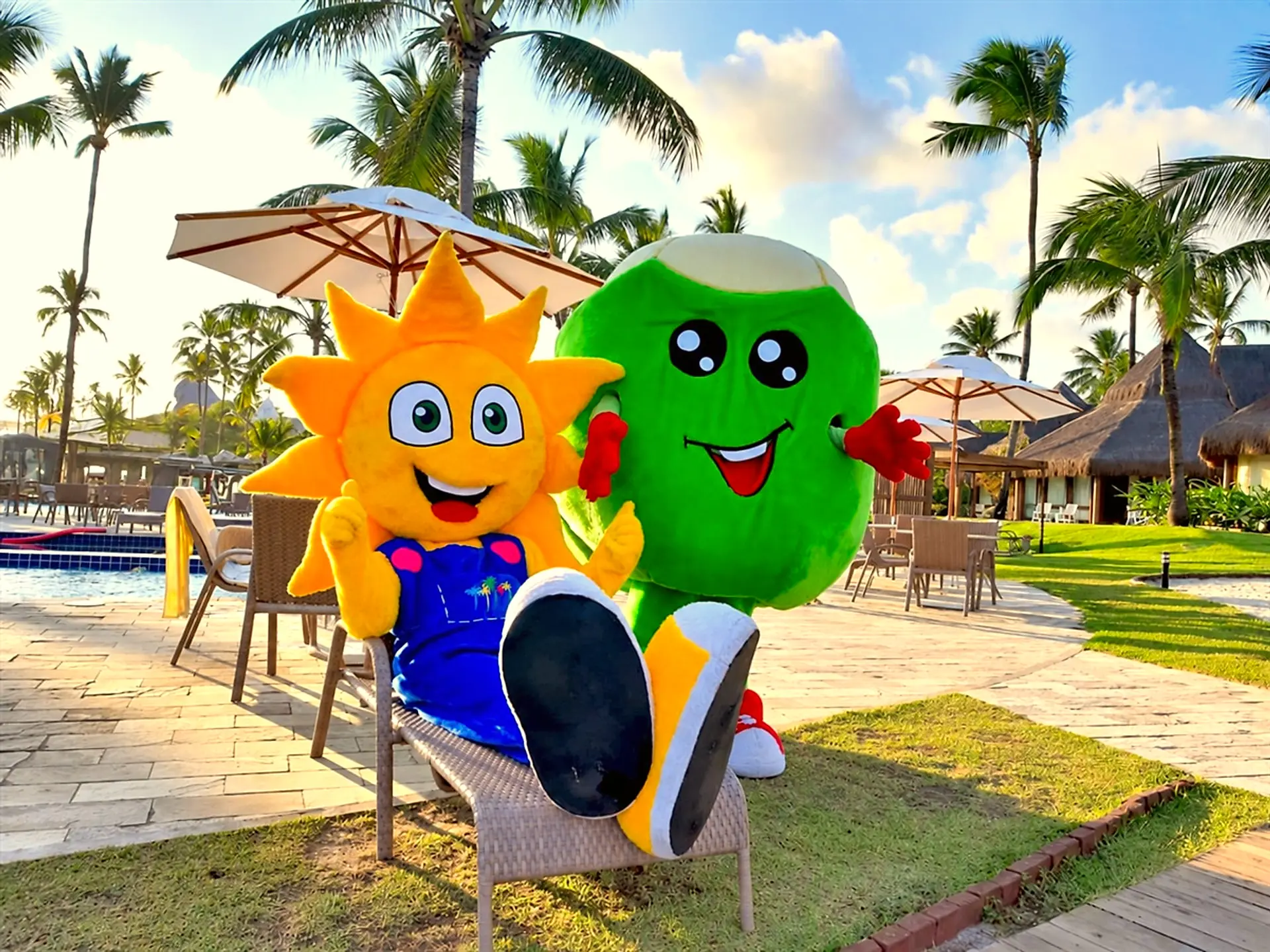 Dois mascotes da Turma do Summy, o sol e o coco, sentados perto da piscina