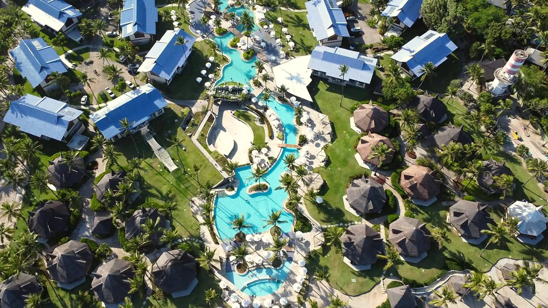 Vista aérea vertical dos jardins, com piscinas, pontes e construções de telhado azul