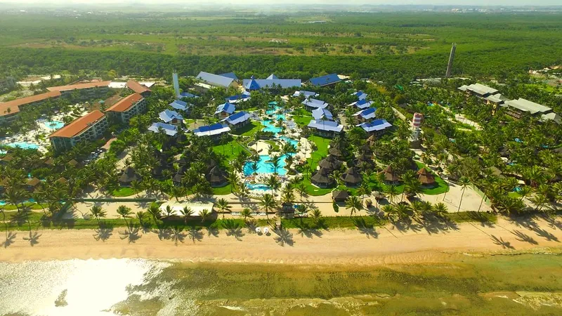 Vista aérea do resort à beira-mar, com a faixa de areia, os jardins e as piscinas entre os coqueiros